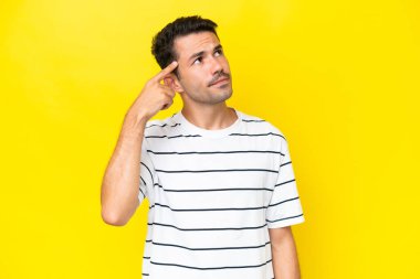 Soyutlanmış sarı arka planda genç yakışıklı adam deliliğin jestini yapıyor. Parmağını kafanın üstüne koyuyor.