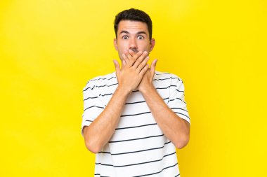 Elleri ile ağız kapsayan izole sarı arka plan üzerinde Genç yakışıklı adam