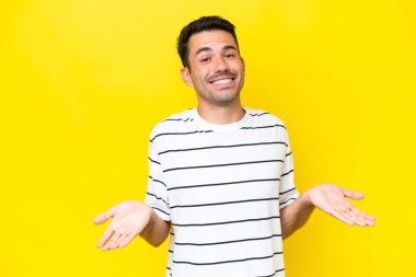 Genç yakışıklı adam izole edilmiş sarı arka planda mutlu ve gülümsüyor.