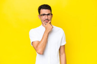 Soyutlanmış sarı arka planı olan yakışıklı bir genç. Şüpheleri var.