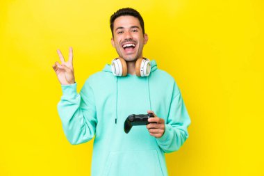 Genç yakışıklı bir adam, izole duvarın üzerinde video oyunu kontrolörüyle oynuyor. Gülümsüyor ve zafer işareti gösteriyor.