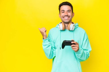 Bir video oyunu kontrolörüyle oynayan yakışıklı genç bir adam izole edilmiş duvarın üzerinde bir ürün sunmak için yan tarafı işaret ediyor.