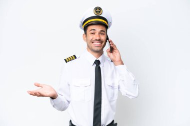 İzole edilmiş beyaz arka plan üzerinde uçak pilotu cep telefonuyla birileriyle sohbet ediyor.