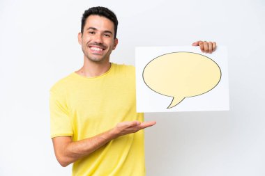 İzole edilmiş beyaz arka plan üzerinde genç yakışıklı bir adam elinde konuşma balonu ikonu olan bir pankart tutuyor ve onu işaret ediyor.