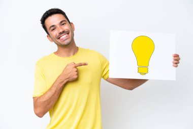 İzole edilmiş beyaz arka planda genç yakışıklı bir adam elinde ampul simgesi olan bir pankart tutuyor ve ona doğrultuyor.