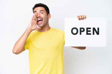 İzole edilmiş beyaz arka planda genç yakışıklı bir adam. Elinde açık yazılı bir pankart var ve bağırıyor.