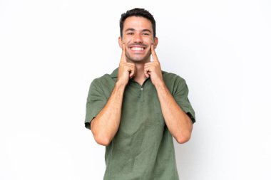 Soyutlanmış beyaz arka planı olan yakışıklı genç adam mutlu ve hoş bir ifadeyle gülümsüyor.