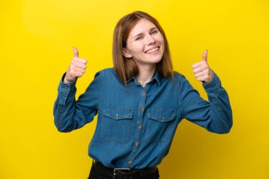 Sarı arka planda izole edilmiş genç bir İngiliz kadın baş parmak işareti yapıyor.