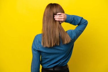 Genç İngiliz kadın arka planda sarı arka planda izole edilmiş ve düşünüyor