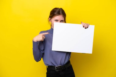 Sarı arka planda izole edilmiş genç bir İngiliz kadın boş bir levha tutuyor ve arkasında saklanıyor.