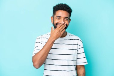 Mavi arka planda izole edilmiş genç Brezilyalı adam mutlu ve gülümsüyor.