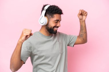 Genç Brezilyalı adam pembe arka planda izole edilmiş müzik ve dans dinliyor.