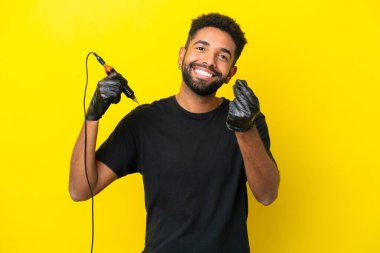 Dövme sanatçısı Brezilyalı adam sarı arka planda izole edilmiş, para hareketi yapıyor.