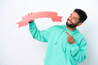 Genç Brezilyalı bir adam beyaz arka planda izole edilmiş, elinde boş bir levhayla onu işaret ediyor.