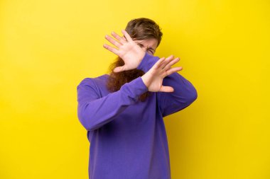 Sarı arka planda sakallı kızıl saçlı adam ellerini öne uzatıyor.