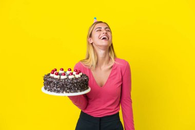 Sarışın Uruguaylı kız sarı arka planda izole edilmiş doğum günü pastası tutuyor ve gülüyor.