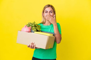 Genç Uruguaylı kız, sarı arka planda izole edilmiş şeylerle dolu bir kutuyu kaldırırken mutlu ve gülümseyen bir ağızla el ele tutuşuyor.