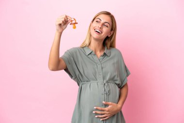 Genç Uruguaylı kadın mavi arka planda izole edilmiş hamile ve emzik taşıyor.