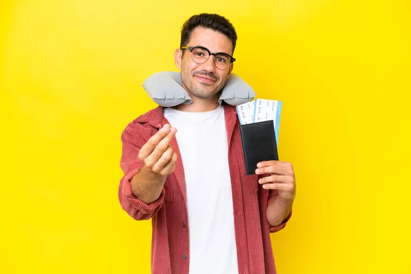 Young handsome man with Inflatable Travel Pillow over isolated yellow background making money gesture