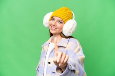 Sarışın bir kadın, izole edilmiş krom arka plan üzerinde kışlık manşetler takıyor ve parmağını kaldırıyor.