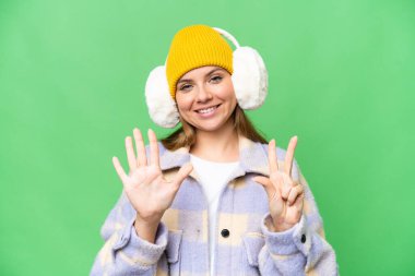 İzole edilmiş krom arka plan üzerinde kışlık manşet takan genç sarışın kadın parmaklarıyla sekiz tane sayıyor.