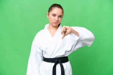 Karate yapan genç sarışın kadın izole edilmiş krom anahtar zemin üzerinde başparmağın olumsuz ifadesini gösteriyor.