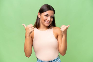 Yeşil krom arka planda izole edilmiş genç beyaz kadın. Baş parmakları havada ve gülümsüyor.