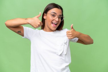 Yeşil krom arka planda izole edilmiş genç beyaz bir kadın baş parmak hareketi yapıyor.