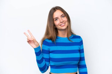 Beyaz arka planda izole edilmiş genç beyaz kadın gülümsüyor ve zafer işareti gösteriyor.