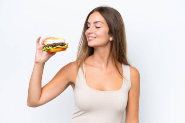 Genç, güzel bir kadın elinde hamburgerle beyaz arka planda mutlu bir ifadeyle.