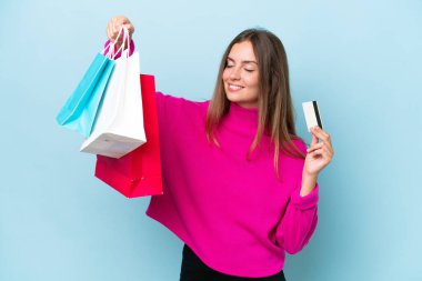 Mavi arka planda izole edilmiş genç bir kadın elinde alışveriş çantaları ve bir kredi kartı tutuyor.