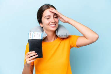 Şişirilebilir seyahat yastığı olan genç ve güzel bir kadın mavi arka planda izole edilmiş, gülümsüyor.