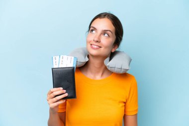 Şişirilebilir seyahat yastığı olan genç ve güzel bir kadın mavi arka planda izole edilmiş bir şekilde yukarı bakarken bir fikir düşünüyor.