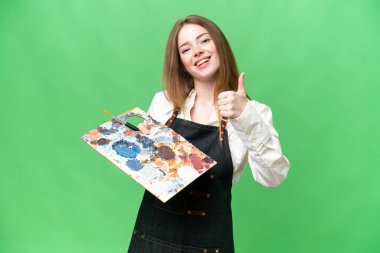 İzole edilmiş krom anahtar zemin üzerinde palet tutan genç bir sanatçı kadın. Başparmaklar yukarı çünkü iyi bir şey oldu.