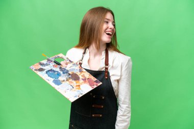 Yanal pozisyonda gülerek izole edilmiş krom anahtar arkaplan üzerinde palet tutan genç sanatçı kadın