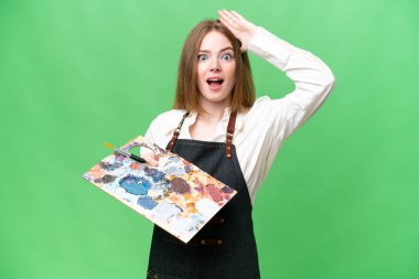 İzole edilmiş krom anahtar arkaplan üzerinde palet tutan genç sanatçı kadın sürpriz bir ifadeyle