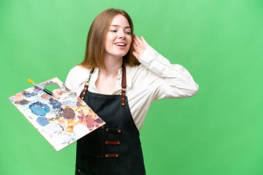 Genç bir sanatçı arka planda bir palet tutuyor. Kulağına elini sürerek bir şey dinliyor.