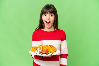İzole edilmiş krom arka planda waffle tutan küçük bir kız. Sürpriz yüz ifadesi var.