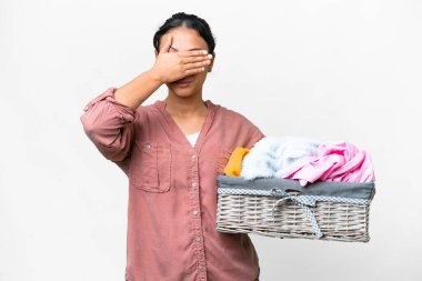 Young Uruguayan woman holding a clothes basket over isolated white background covering eyes by hands. Do not want to see something