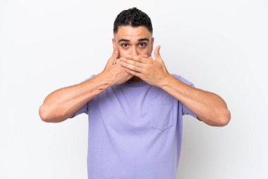 Beyaz arka planda izole edilmiş genç Arap yakışıklı adam elleriyle ağzını kapatıyor.