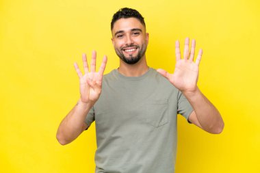 Sarı arka planda izole edilmiş genç Arap yakışıklı dokuz parmaklı sayıyor.