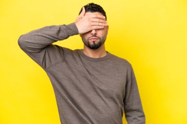 Sarı arka planda izole edilmiş genç Arap yakışıklı adam gözlerini elleriyle kapatıyor. Bir şey görmek istemiyorum.