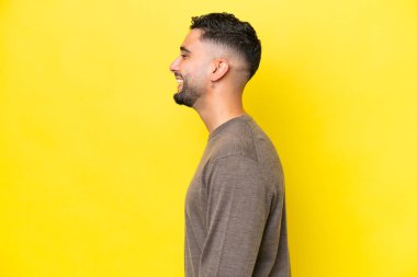 Sarı arka planda yalnız yaşayan yakışıklı genç Arap adam yan yana gülüyor.