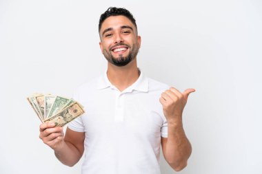 Genç Arap bir adam beyaz arka planda izole edilmiş bir sürü para alıyor. Bir ürünü sunmak için kenarı işaret ediyor.