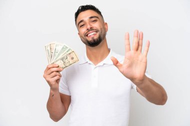 Genç bir Arap, beyaz arka planda izole edilmiş bir sürü para alıyor. Beş parmaklı sayıyor.
