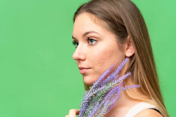 Young blonde woman over isolated chroma key background holding a lavender plant. Close up portrait