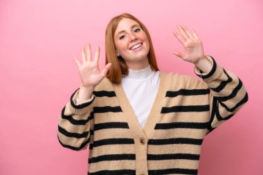 Pembe arka planda izole edilmiş genç kızıl saçlı kadın parmaklarıyla ona kadar sayıyor.