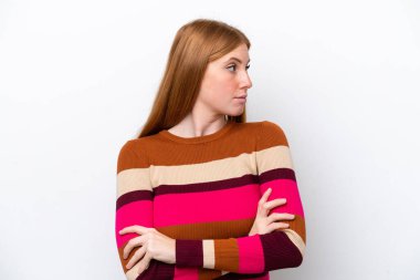 Beyaz arka planda izole edilmiş genç kızıl saçlı kadın kollarını çapraz tutuyor.