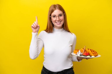 Sarı arka planda gözleme tutan genç kızıl saçlı kadın harika bir fikre işaret ediyor.