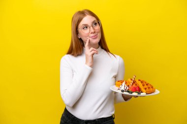 Sarı arka planda gözleme tutan genç kızıl saçlı kadın yukarı bakarken bir fikir düşünüyor.